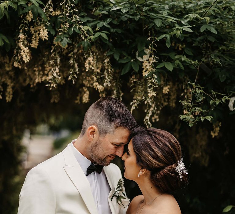 The bride wears an off the shoulder lace wedding dress smiling up at the groom in a white tuxedo 