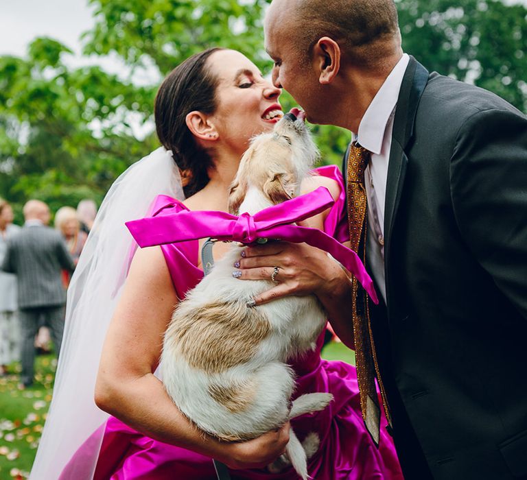 Bride in off the shoulder front ruching pink Vivienne Westwood wedding dress and two layer white and pink ombre veil holding Dolly the dog wearing large pink satin bow 