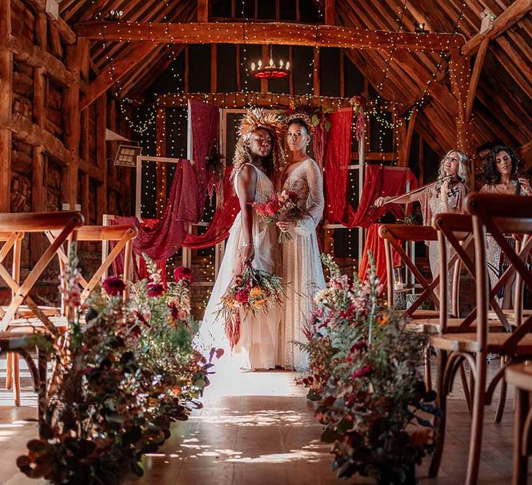 Brides in complimenting boho wedding dresses with embroidered stars and polka dots and gold bridal crowns kissing in front of large orange smoke bomb at Silchester Farm