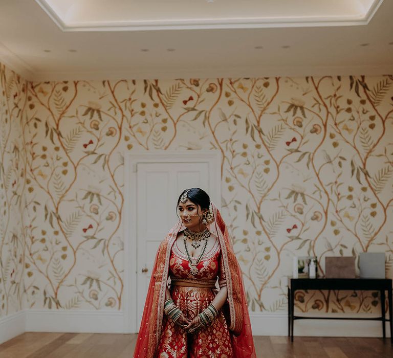 South East Asian bride wears bangles, red and gold lehenga and intricate henna across her hands 