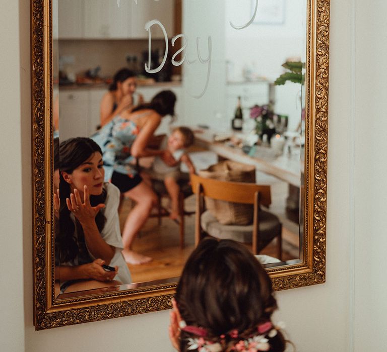 Bride does her own wedding makeup in a gold edged mirror with wedding day written in white pen 