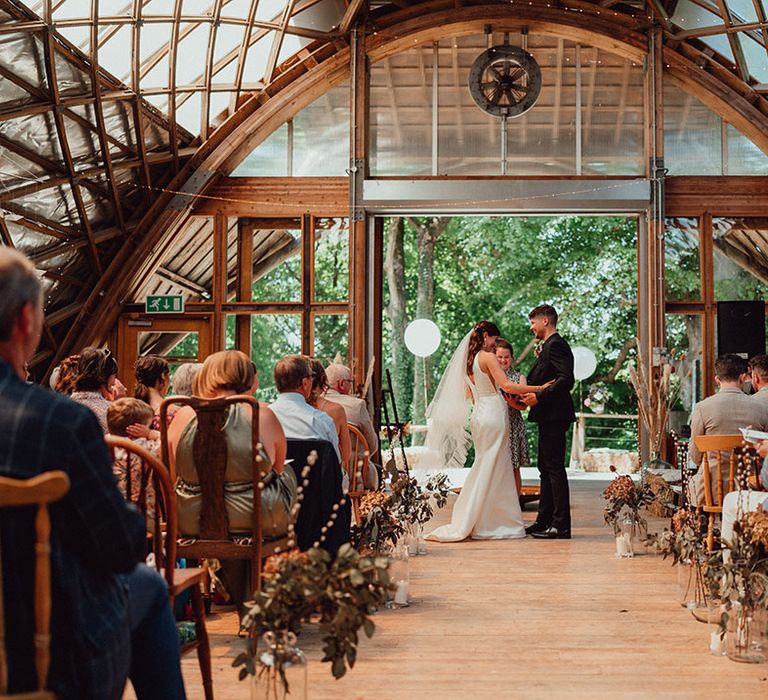 Bride and groom stand together at the altar for their wedding baptism ceremony with neutral orange wedding flowers lining the aisle 