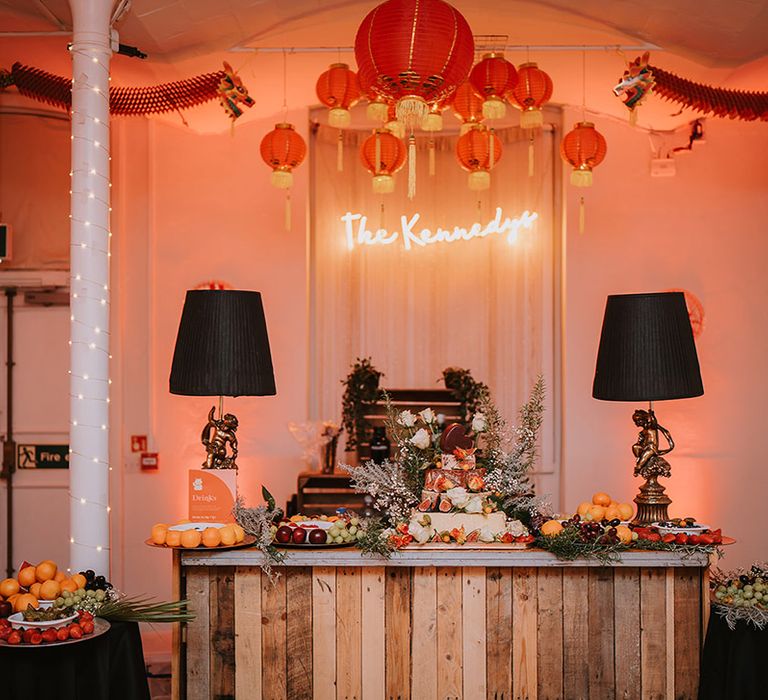 Wedding cheese tower with foliage, baby's-breath and seasonal fruit decorations at London wedding with Chinese lanterns hanging above and personalised neon light