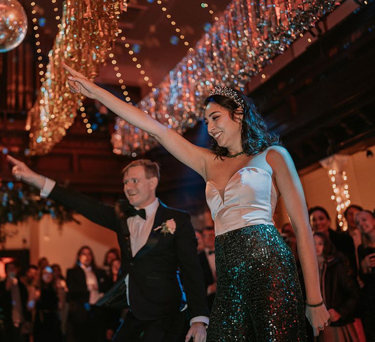 Bride in taffeta sweetheart neckline wedding top and dark green sequin disco trousers and groom in black tux having a dance at their wedding disco