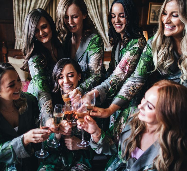 Bridesmaids in grey patterned robes with flower print cheers each other and the bride as they get ready on the morning of the wedding 