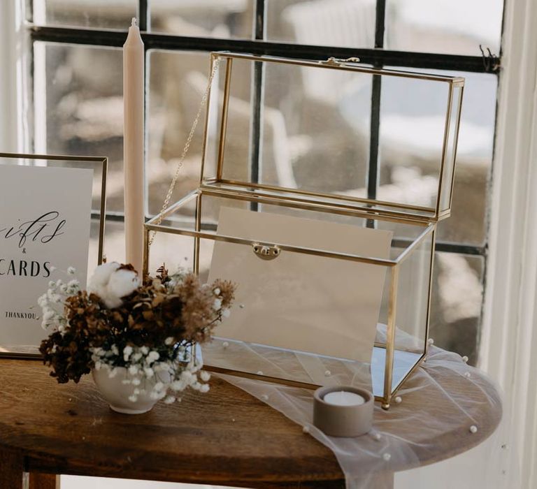 Elegant minimalistic wedding decor - glass box with wedding stationery gift cards in them next to a framed sign and pot of roses, carnations and baby's-breath 