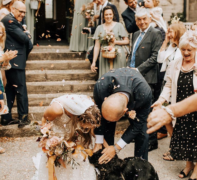 The bride and groom, who are vets, share their fun confetti exit with their pet dog with a shiny black coat in Cheshire 