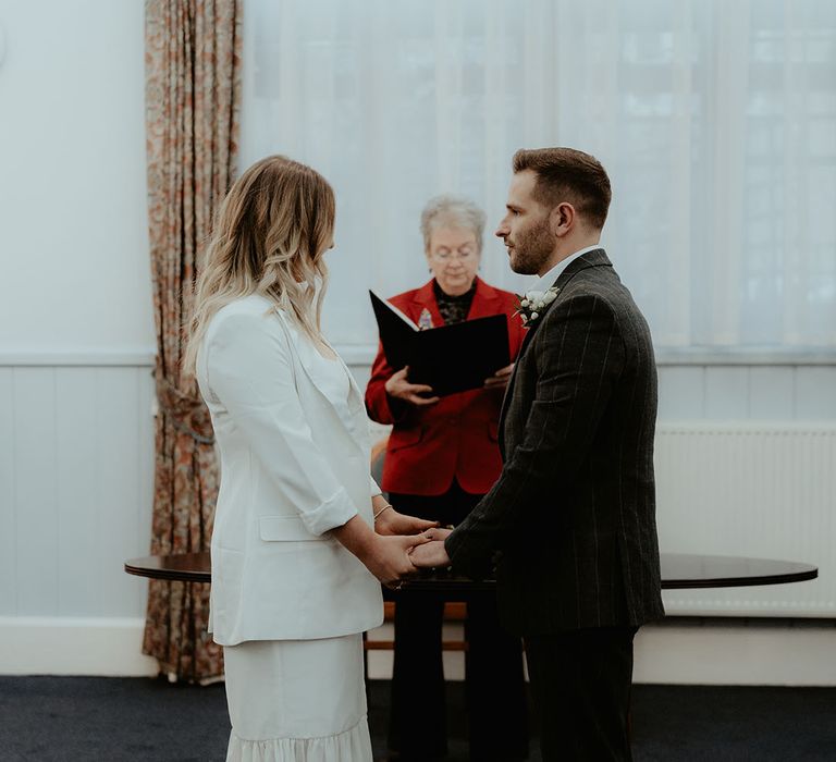 Groom in grey checkered suit stands at the altar with the bride in a white blazer and ruffle wedding dress with pointed toe wedding shoes for Stroud Registry Office wedding 