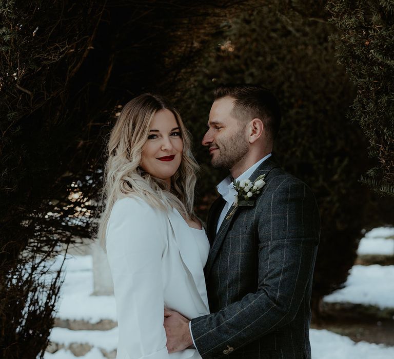 The bride smiles at the camera with bright red lipstick in ruffle wedding dress with groom in checkered suit for winter wedding 