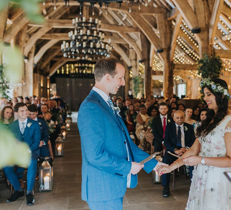 Bride in a floral wedding dress and groom in a blue suit exchanging personalised wedding vows 