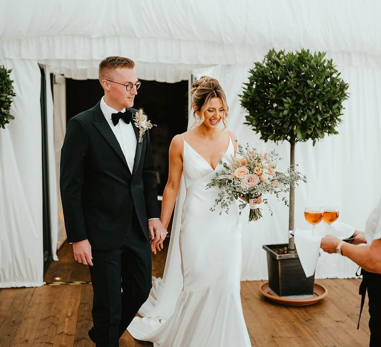 White marquee wedding reception for the Elms Barn wedding with the bride carrying her pink rose and white gypsophila bouquet with bunny grass 