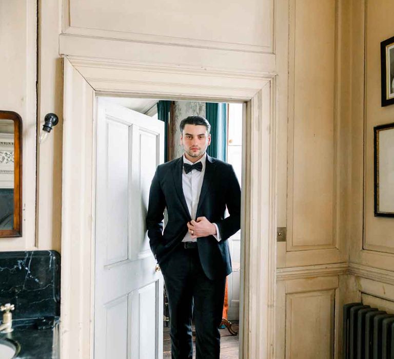 Groom in classic black tuxedo and black bowtie walking through the door at St Giles House 