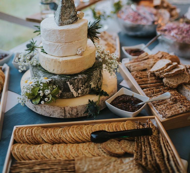 Trays of crackers and bread with bowls of chutney surround the epic cheese tower decorated with flowers for rustic marquee wedding at Badgers Holt