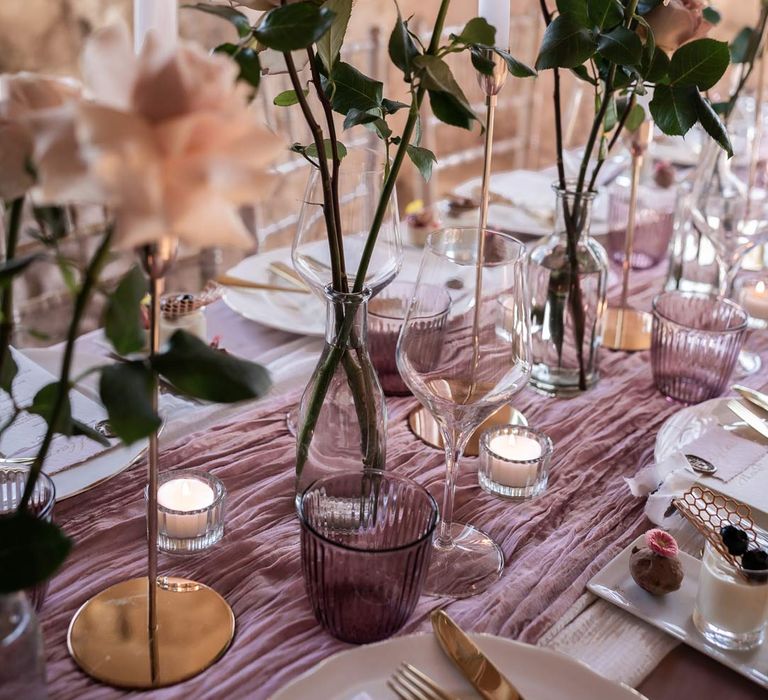 Garden rose wedding centrepieces on lavender tablecloth with lilac tulle table runner, tea light candles and white tapered candles 