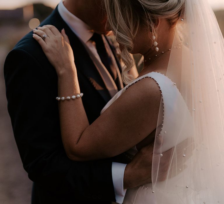 Bride wearing pearl wedding veil, pearl earrings, bracelet and necklace with the groom at golden hour 