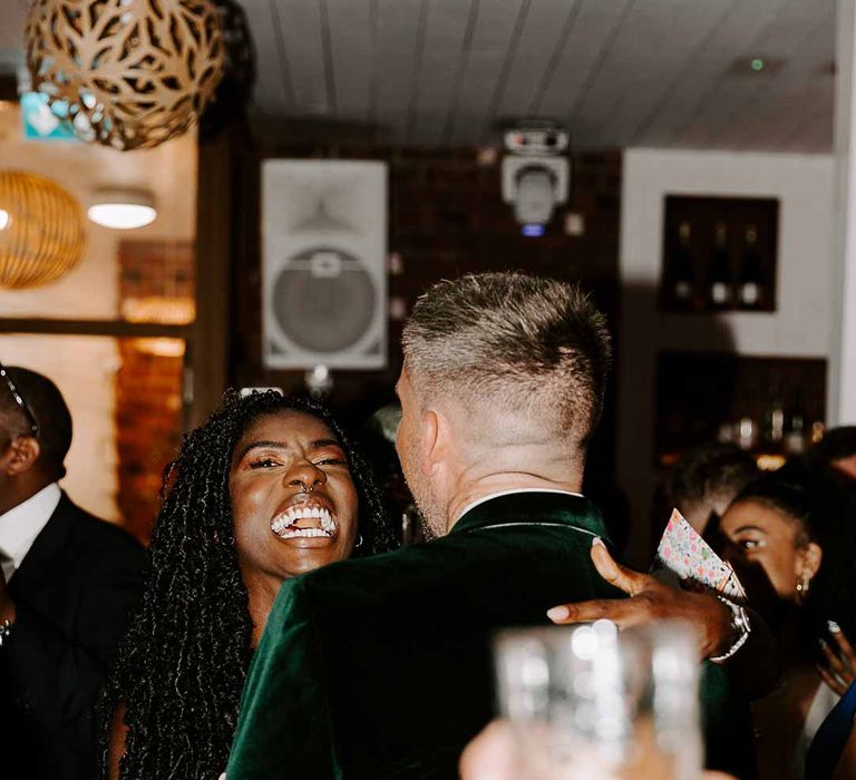 Bride laughing over the shoulder of groom in bottle green velvet grooms blazer during upbeat first dance wedding song 