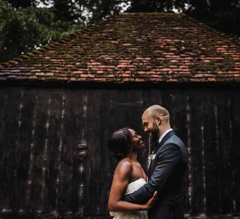 Bride in sweetheart neckline lace wedding dress and groom in classic black three piece grooms suit with bow tie and white rose and foliage boutonniere in church embracing