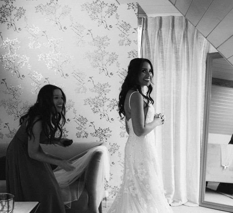 Bridal preparations - bridesmaid helping bride in her a-line tulle wedding dress with beaded lace applique with petals and a square neckline with side tulle cutouts