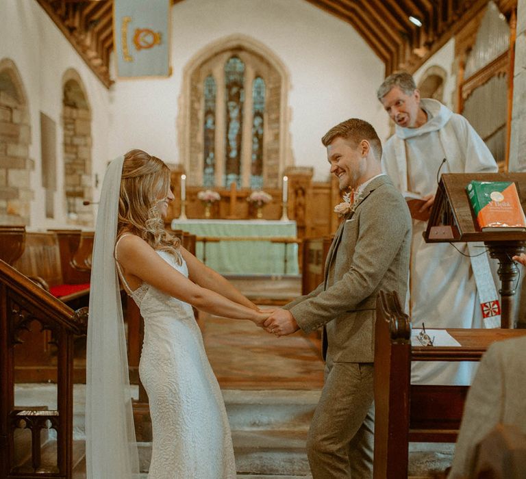 Bride with half up half down wedding hair in classic fitted wedding dress and long veil with the groom in grey suit for church wedding 