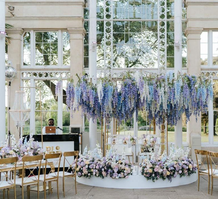 Syon Park wedding venue reception room with gold chairs, botanical tablescapes with large pastel flower centrepieces and suspended pastel foliage decor 