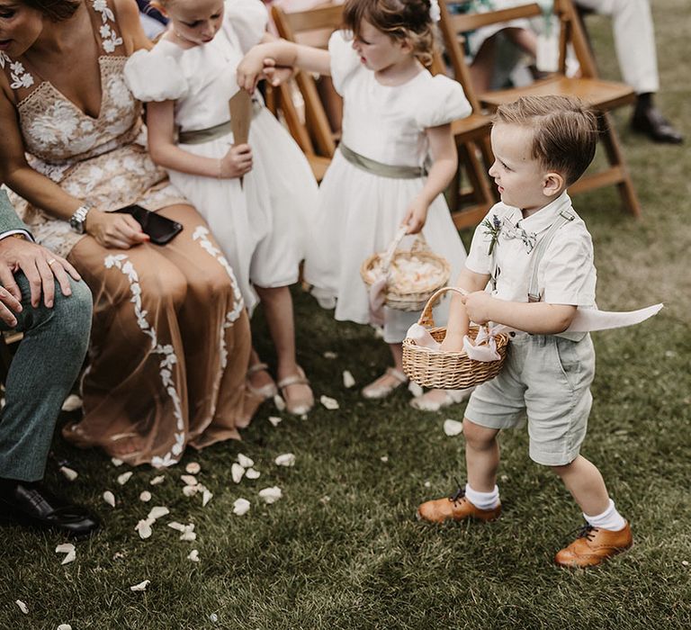 Page boy and flower girl walking down the aisle at outdoor wedding wearing sage green outfits 