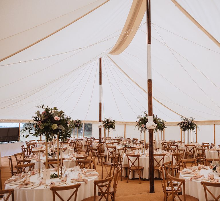 Round tables decorated with tall floral centrepieces at marquee wedding reception 