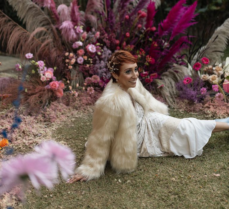 The bride sits down wearing a fluffy white fur jacket cover up for the Brazil wedding 