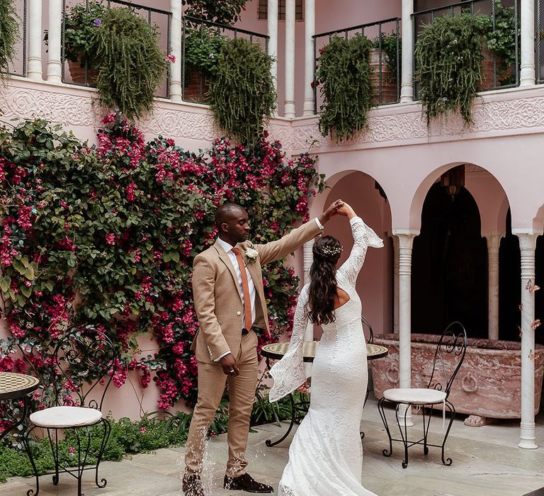 The groom spins the bride around to show off her wedding dress surrounded by pink painted scenery 