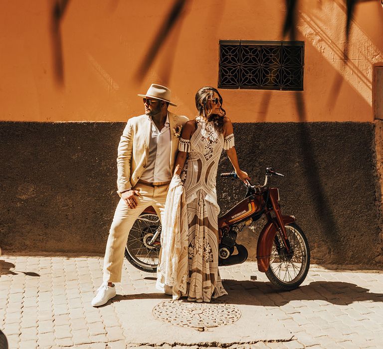 The bride and groom pose in their boho outfits on a motorbike 