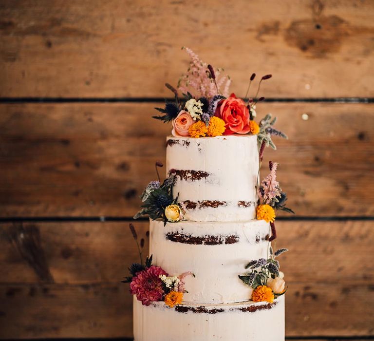 Three tier semi naked wedding cake with red and orange flowers 