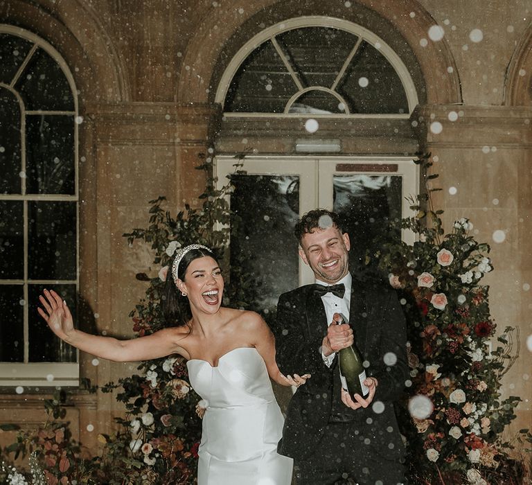 The groom pops and sprays a bottle of champagne to celebrate the wedding with the bride in a mermaid wedding dress 