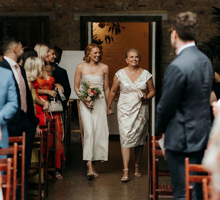 The bridesmaid and the mother of the bride walk down the aisle together 