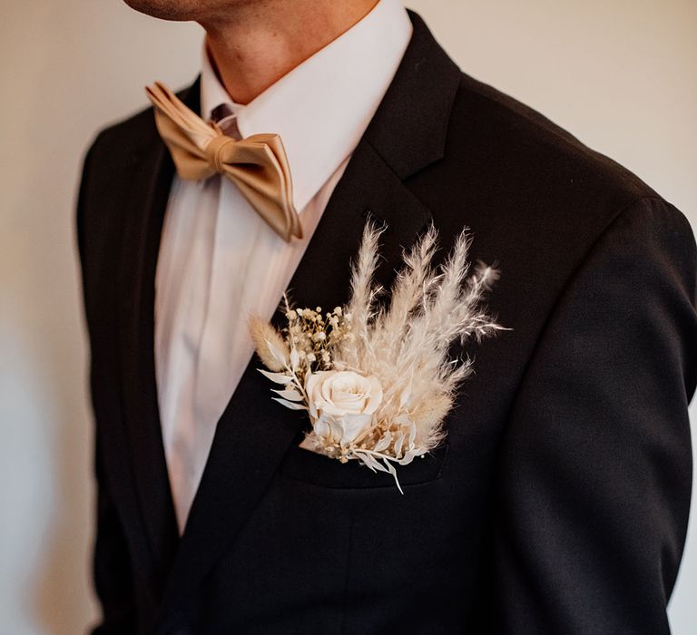 Groom wearing Hugo Boss wedding suit with champagne coloured bow tie with an all white dried flower buttonhole 