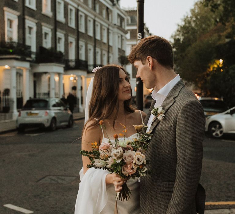 Bride in slip wedding dress holding a pink bouquet looking at her groom 