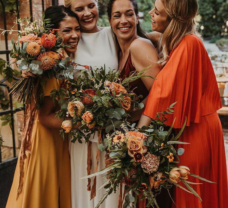 Bridal party in earthy toned dresses hugging 