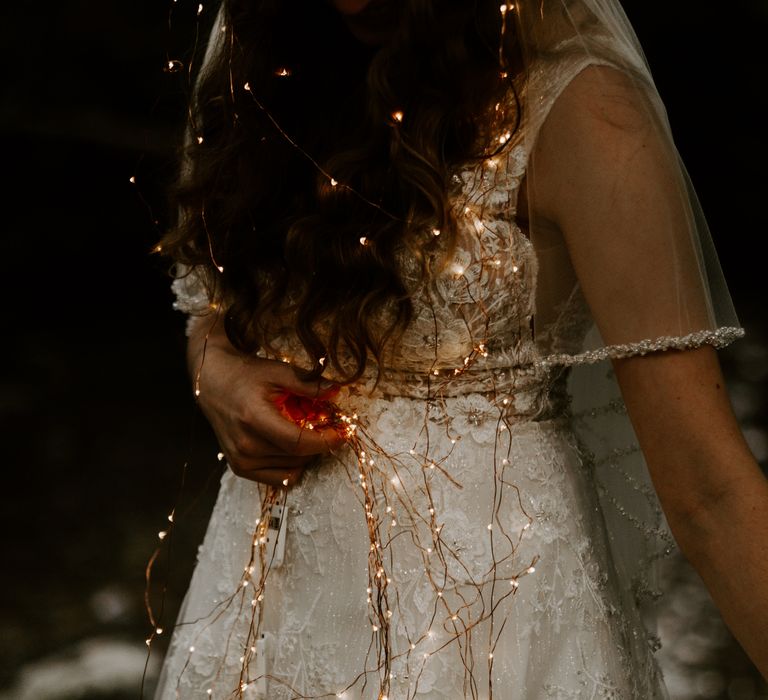 Bride is draped in string fairy lights that highlight the beaded dress and veil 