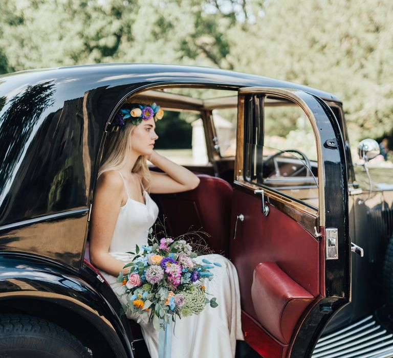 Bride in a satin wedding dress with colourful flower crown and matching bouquet of pink, purple, orange and blue assorted flowers 