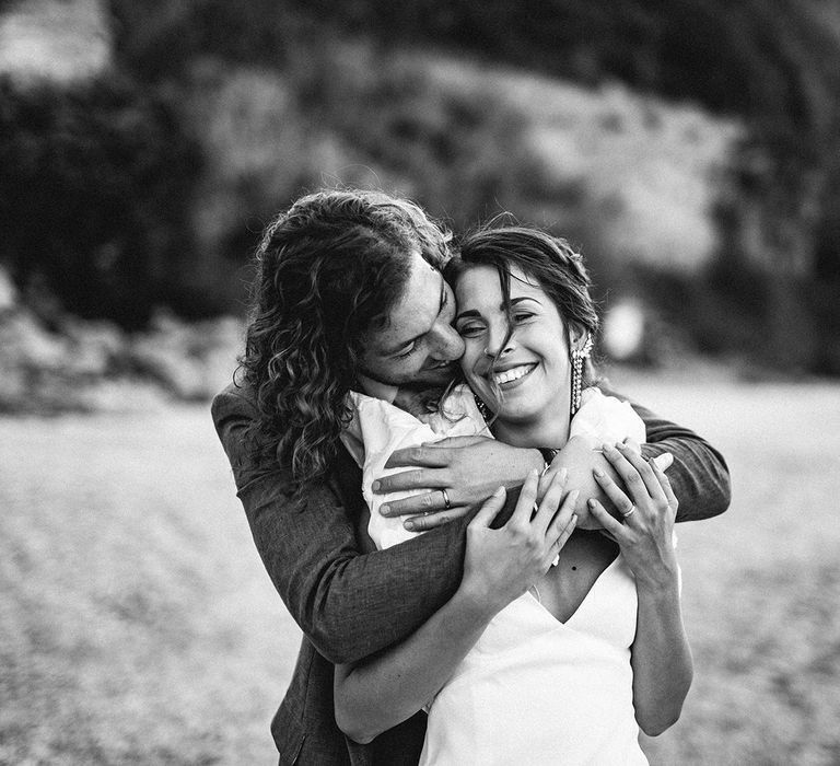 Groom with curly hair embracing his bride in a ruffle sleeve wedding dress on the beach in Italy 