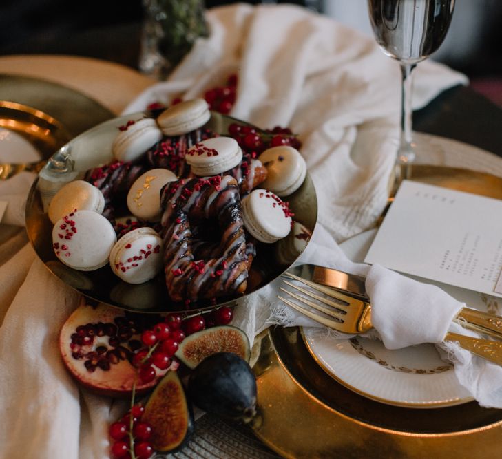 A table set up with gold cutlery and a selection of deserts including macarons. Photography by Rebecca Goddard.