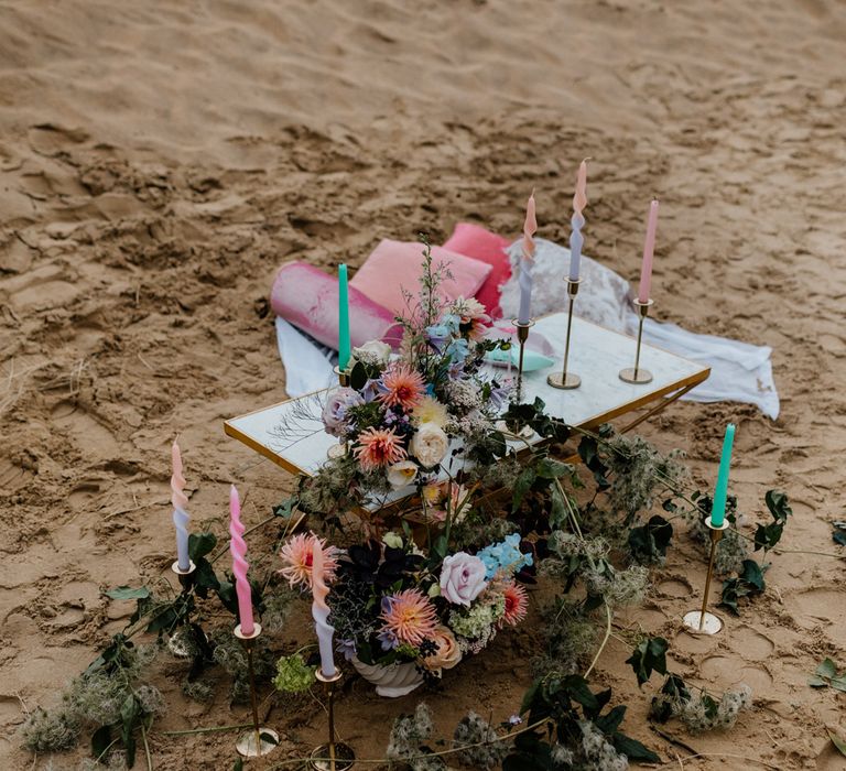 Intimate picnic table on the beach with pastel coloured flowers, cushions and candles styled by Pink Palms 