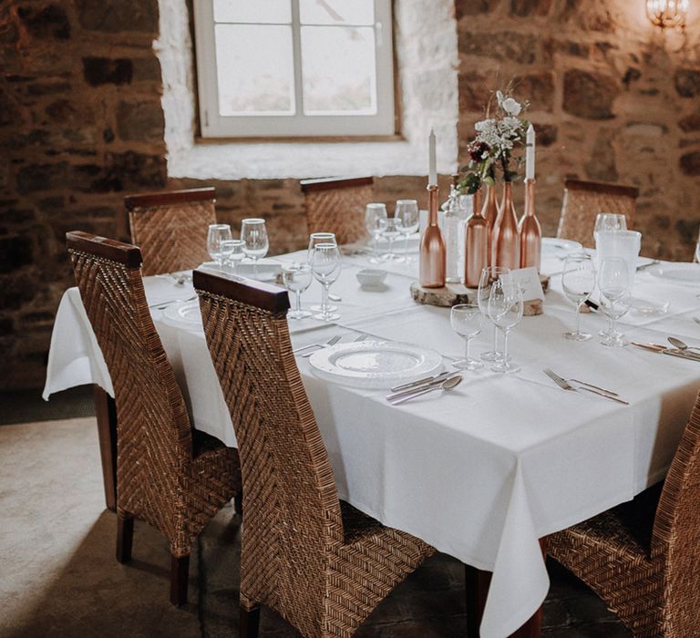 Rustic elegant wedding table decor with rose gold bottle details and rattan chairs at German wedding