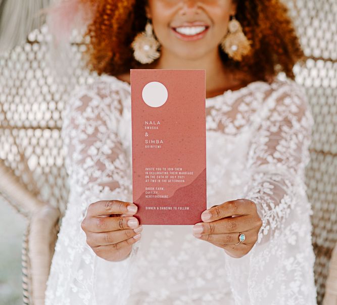 Bride holds up Chloe Ainsley Creative Stationery to the camera whilst smiling