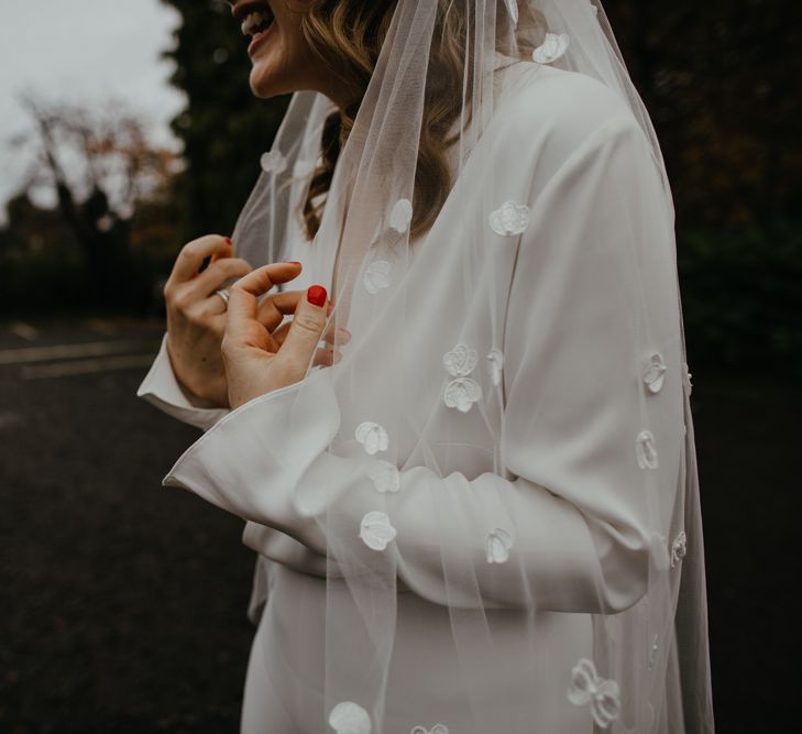 Bride with bright red nail polish holding her appliqué wedding veil 