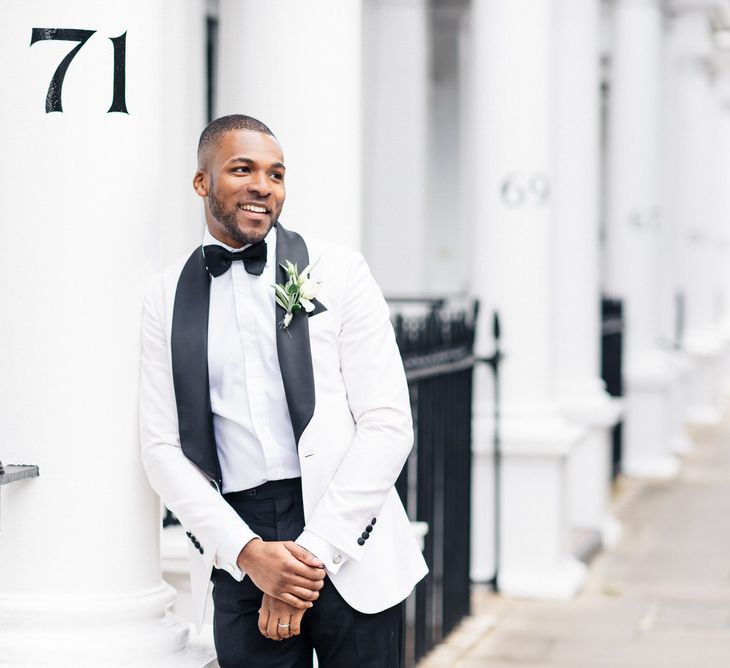 Groom leans against white pillar wearing monochrome tux