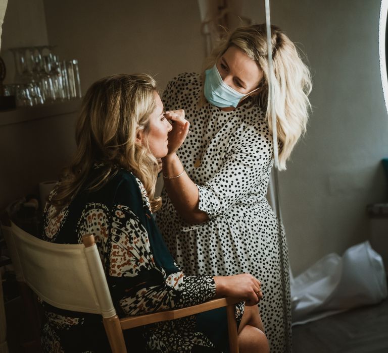 Blonde bride sits in chair as she has her makeup applied