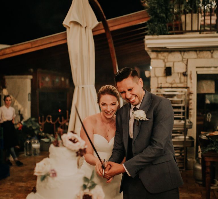 Bride and groom cutting into a huge four tier white wedding cake with a sword