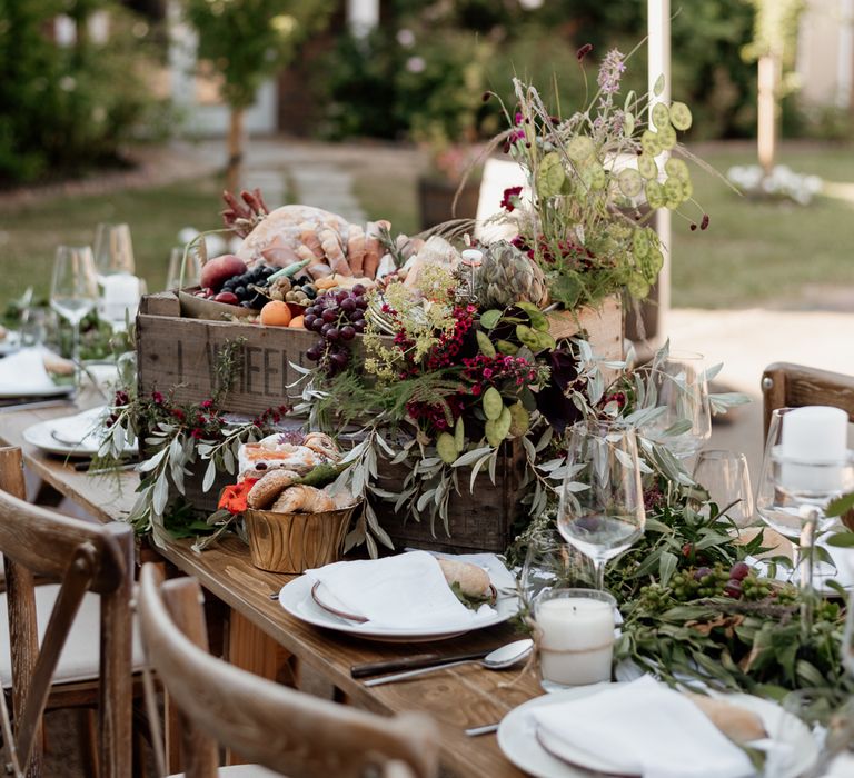 Outdoor grazing table in rustic setting surrounded by green florals and wooden table