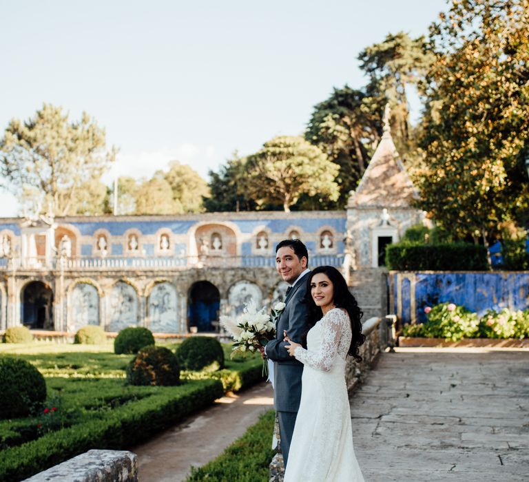 Bride & groom look toward camera as they smile on their wedding day whilst outdoors in Lisbon