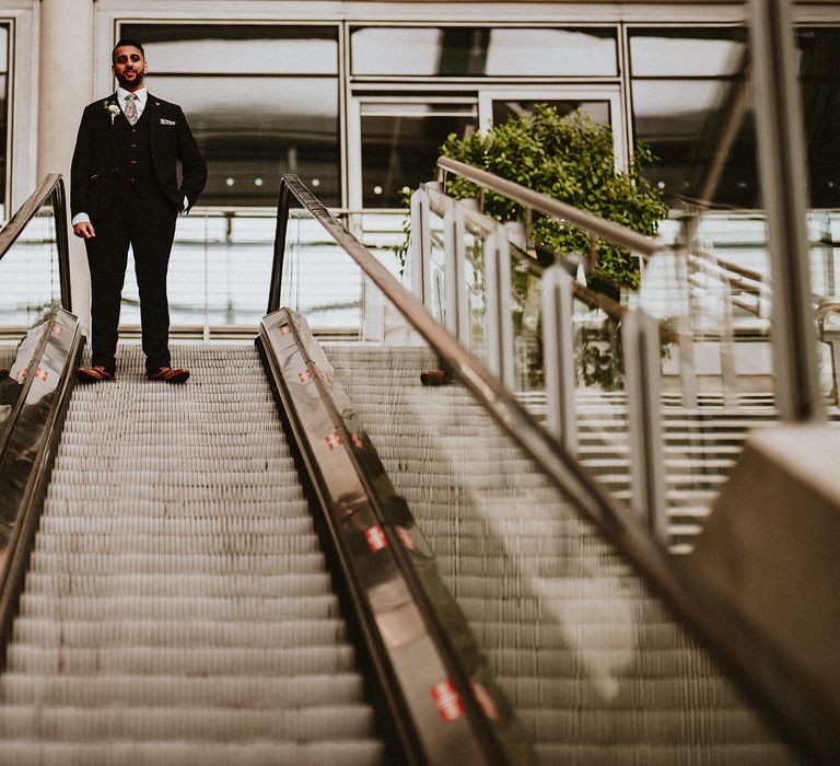 Groom in a three-piece suit with floral tie standing on the escalator at Brent Civic Centre 