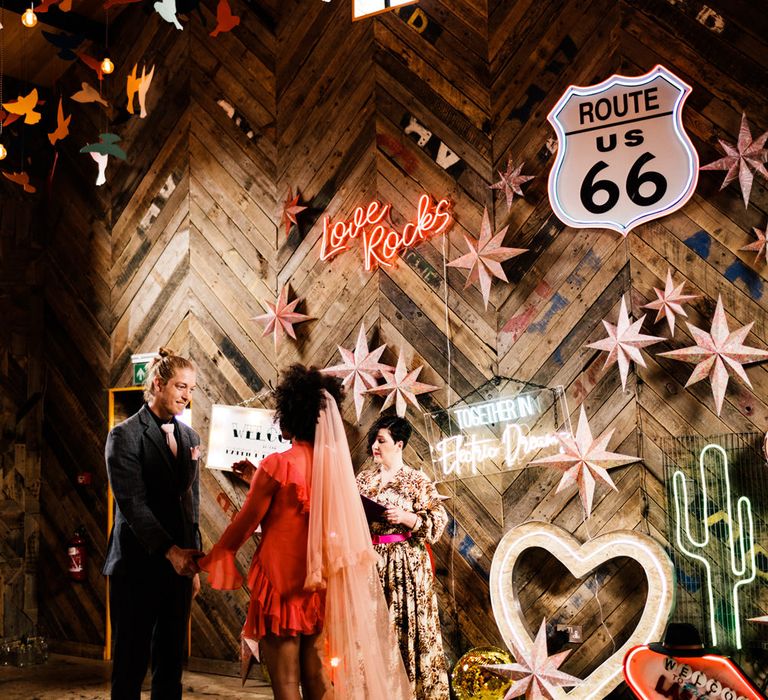 Bride in a red short wedding dress and long pink veil for a stylish wedding in a shed decorated with neon wedding signs 